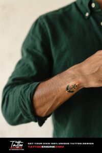 Close-up of a man's wrist with a fine-line anchor tattoo and a dark green shirt.