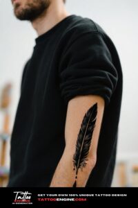A close-up image of a man's forearm with a feather quill tattoo, wearing a black sweatshirt.