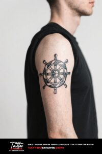 Medium shot of a man's arm with a geometric ship's wheel tattoo in a dark blue t-shirt.