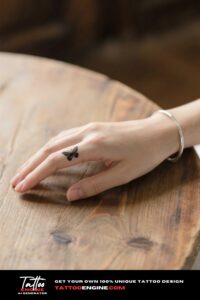 A tiny, minimalist butterfly tattoo on the side of a woman's finger in a cinematic close-up.