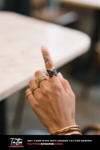A close-up of an outline butterfly tattoo on a woman's thumb with gold rings