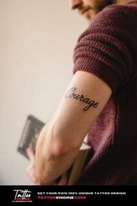 Extreme close-up of a man's inner forearm with a 'Courage' script tattoo, holding a book in a maroon sweater.