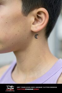 Tiny single-needle crescent moon tattoo behind a teen's ear on tan skin.