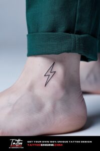 Minimalist black lightning bolt tattoo on a woman's outer ankle, green linen trousers above.