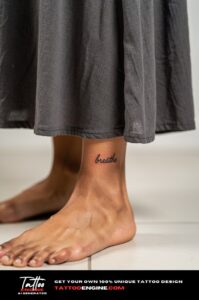 Minimalist 'breathe' script tattoo on woman's ankle, fine black cursive, bare skin.