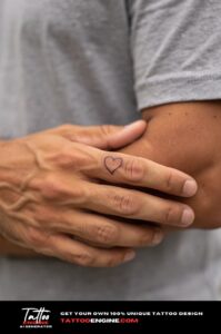 Tiny heart tattoo at the base of a ring finger on olive skin, fine linework.
