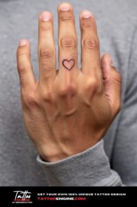 Tiny heart tattoo below the nail on a man's ring finger, in overcast daylight.