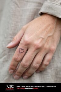 Delicate fine-line heart tattoo on side of ring finger, framed closely on pale skin.
