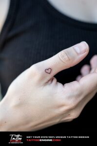 Small minimalist heart outline tattoo on the side of a fair-skinned thumb.