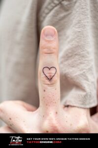 Minimalist heart outline tattoo on outside of ring finger, fine and subtle on fair skin.