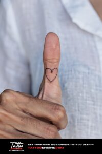 Minimalist script heart tattoo on side of ring finger, subtle and healed on brown skin.