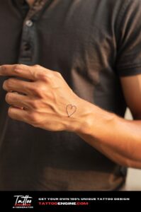 Script-style open heart tattoo on outer index finger, delicate on golden-brown skin.