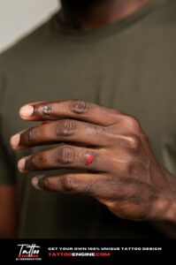 Tiny red heart tattoo on outer pinky finger, bold on dark skin and closely cropped.